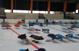 Des dizaines de lits de camps recouverts de duvets sur la patinoire