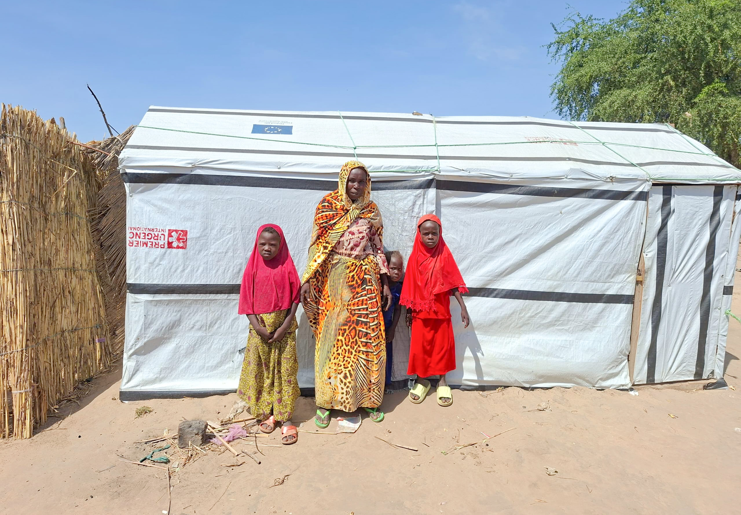 Kambo et trois de ses enfants devant leur abri d’urgence, Blangoua, département du Logone et Chari, Extrême-Nord Cameroun, octobre 2025 | © Première Urgence Internationale 